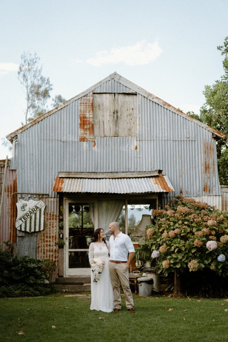 A lovely couple standing in front of the famous barn at their driftwood shed wedding.