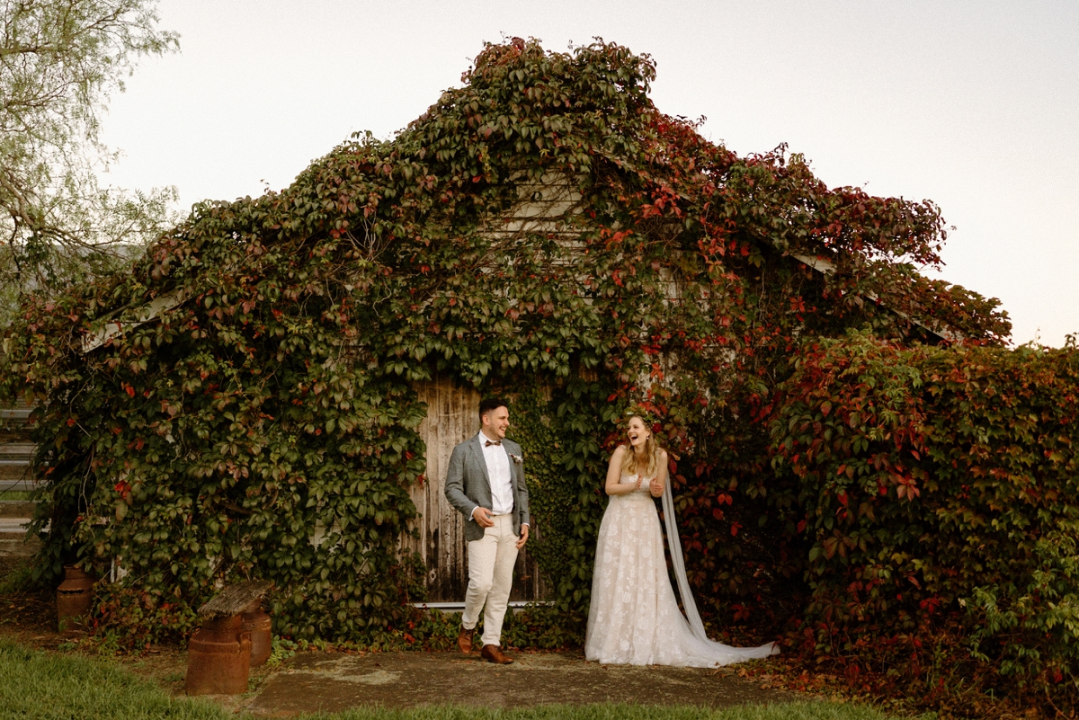 a newly wedded couple laughing in front of an autumn leaved barn at their willow farm wedding in berry