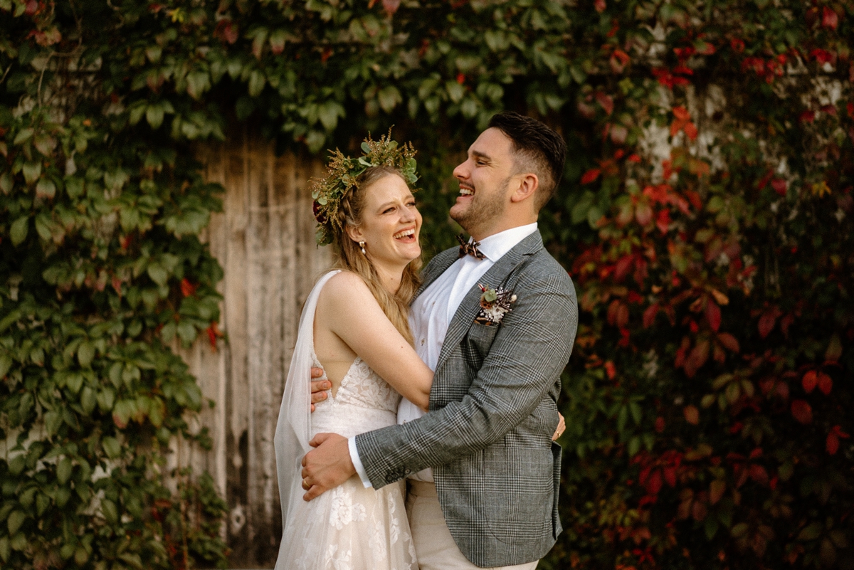 a newly wedded couple laughing in front of an autumn leaved barn at their willow farm wedding in berry