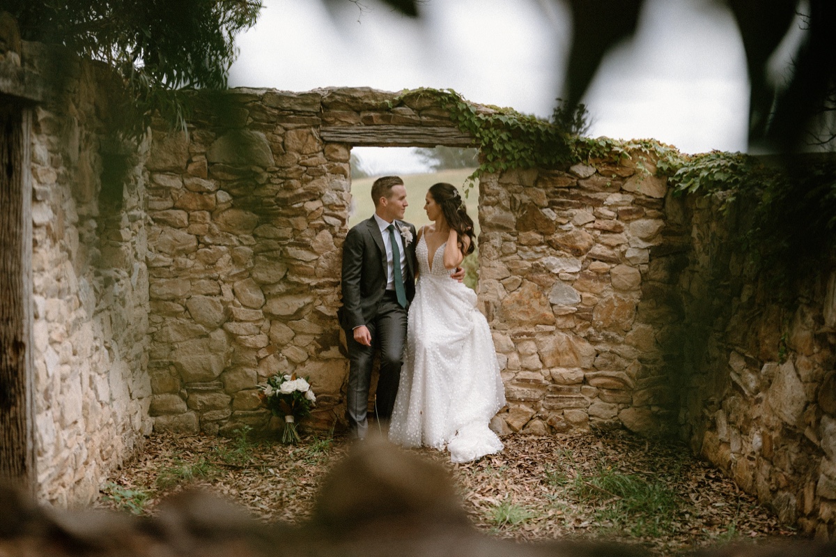 a couple are sitting on an old historic wall at their mali brae farm wedding