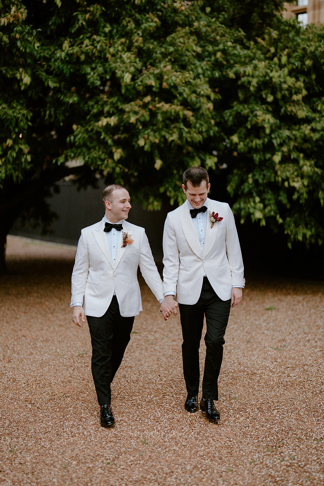 A same sex couple walking in front of a nice green tree at their Sydney Mint wedding.