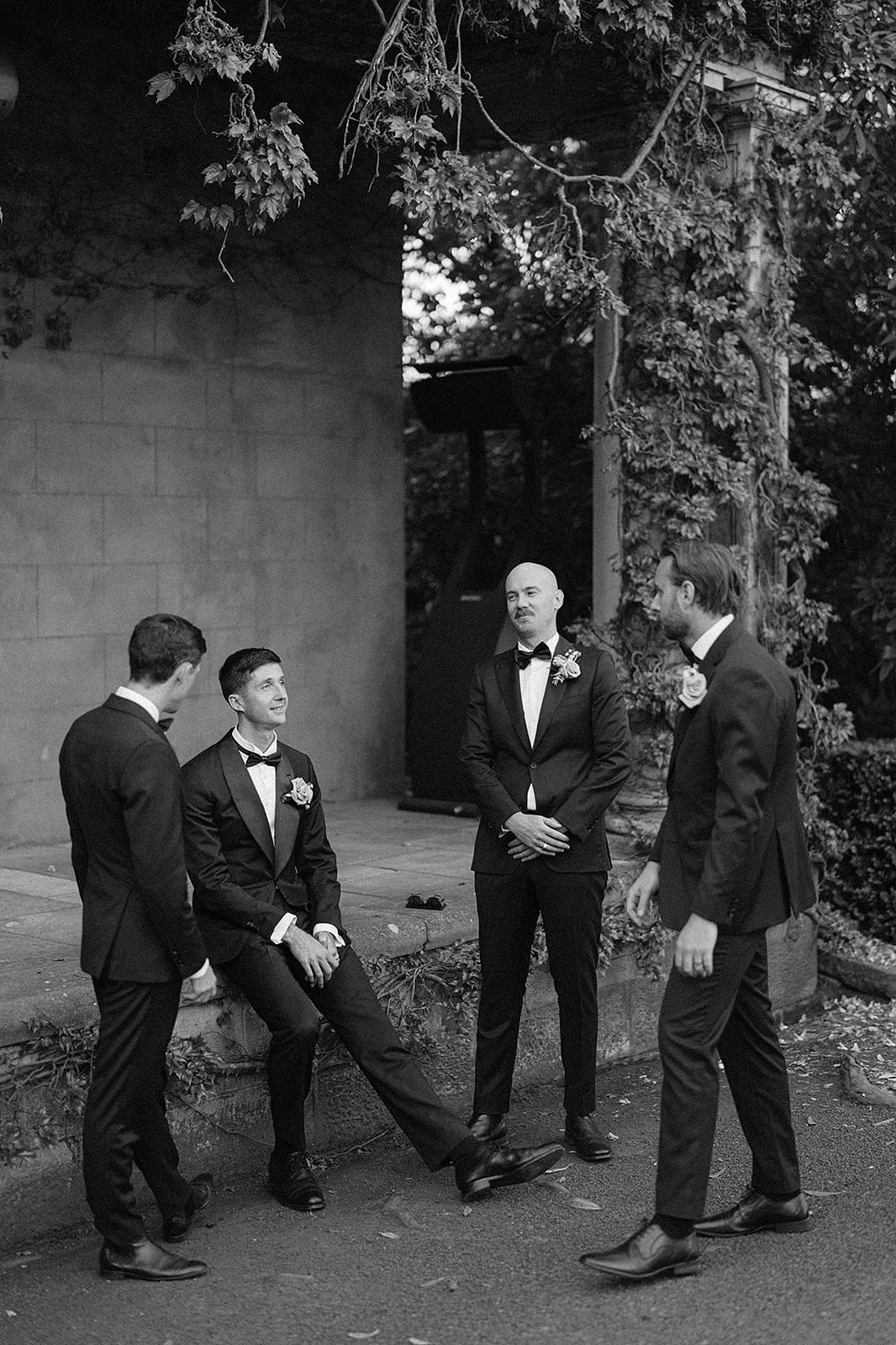 A groom and his groomsmen casually chatting in front of a homestead at his Bendooley Book Barn wedding.