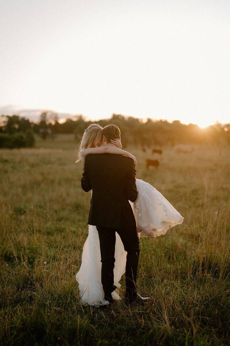 A bride and groom having fun in a field at sunset in front of their southern highlands wedding photographer
