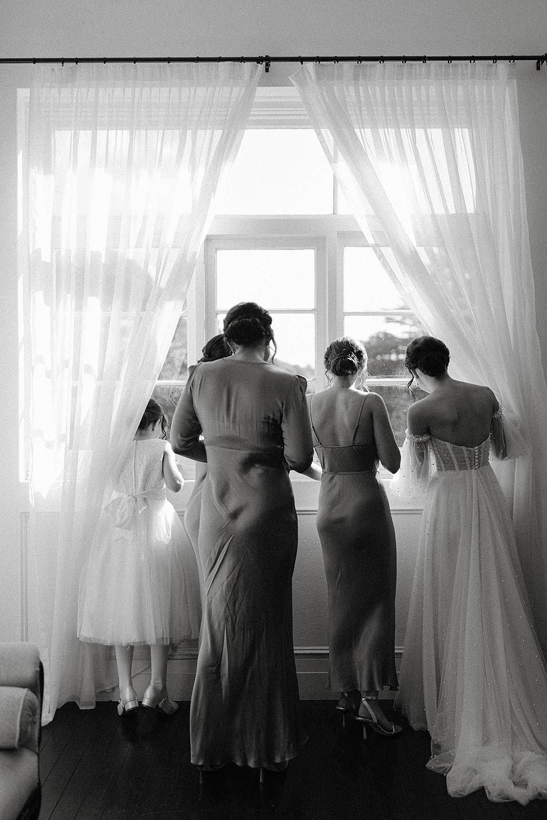 A black and white image shot from behind a few bridesmaids looking out a window for the brides southern highlands wedding at the Robertson Hotel.